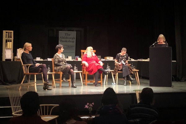 Elizabeth Sennit-Clough, Jacqui Saphra, Amy Key and AK Blakemore sit onstage while Helen Taylor introduces