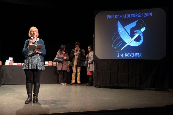 Picture of Jean Sprackland reading on stage with the Poetry in Aldeburgh logo projected behind her